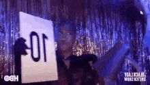 a woman is holding a sign that says `` for '' in front of a tinsel curtain .