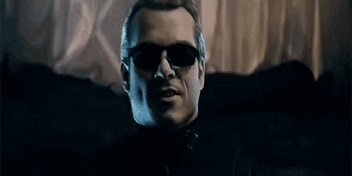 a man wearing sunglasses and a black suit is looking at the camera .