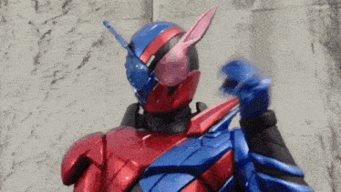 a red and blue robot is standing in front of a wall and making a funny face .
