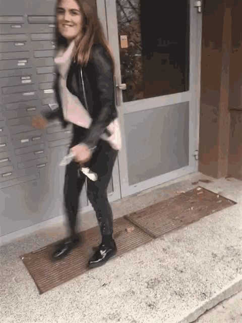 a woman in a leather jacket is standing in front of a building