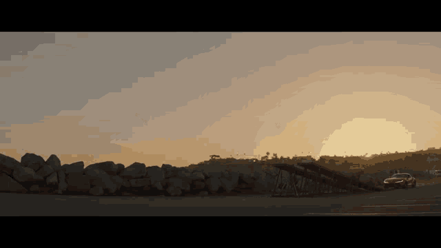 a car is parked in front of a large pile of rocks at sunset