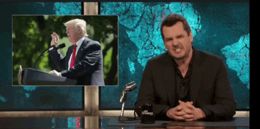 a man is sitting at a desk with a picture of donald trump on the screen behind him .