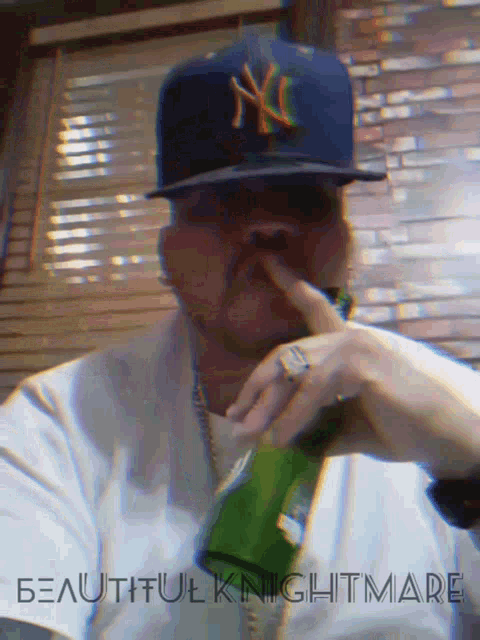 a man wearing a ny hat holds a green bottle