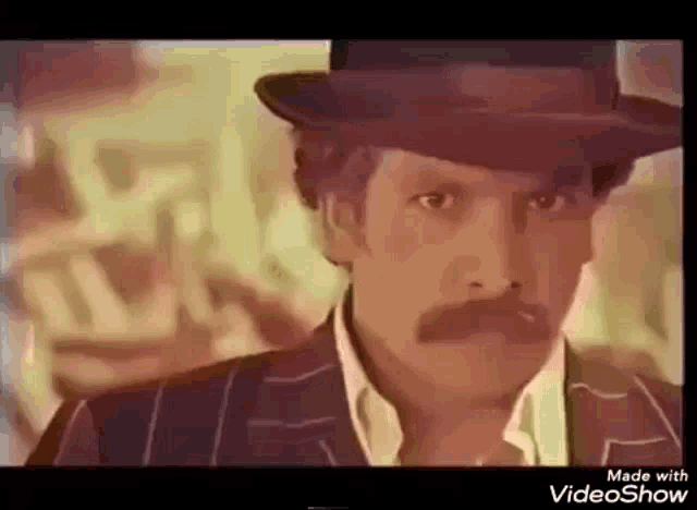 a man with a hat and a mustache is smoking a cigarette .