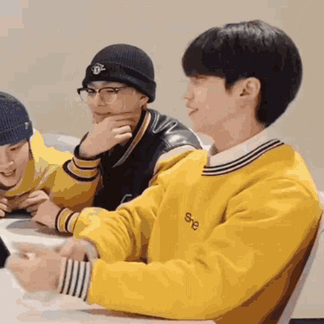 a group of young men are sitting at a table with one wearing a yellow sweater .