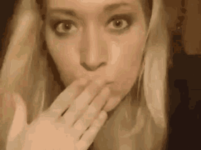 a woman is covering her mouth with her hand while looking at the camera .