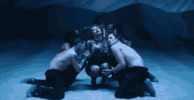 a group of people are kneeling around a woman in a dark room