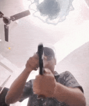 a man is holding a gun in his hands in a room with a ceiling fan .