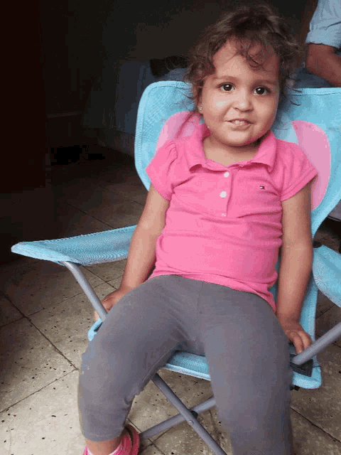 a little girl wearing a pink tommy hilfiger polo shirt sits in a blue chair