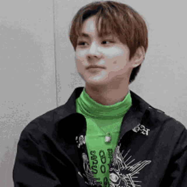 a young man wearing a green turtleneck and a black shirt is looking at the camera .