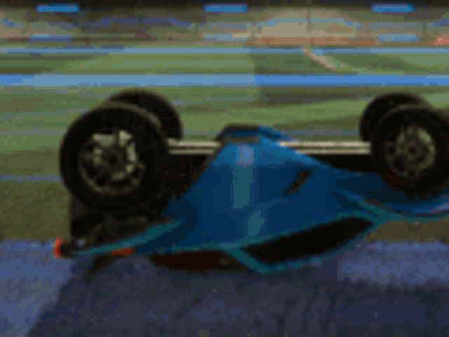 a blue rocket league car is rolling on its side on a soccer field .