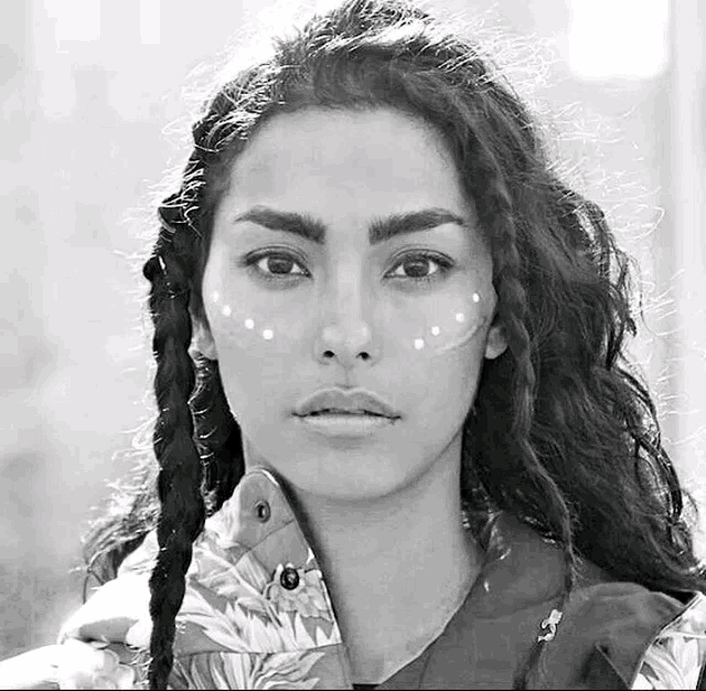 a black and white photo of a woman with dreadlocks and white paint on her face