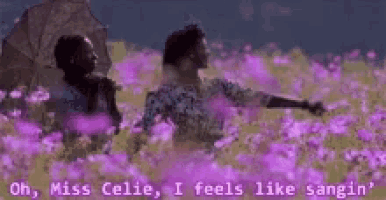 a man and a woman are standing in a field of purple flowers holding umbrellas .