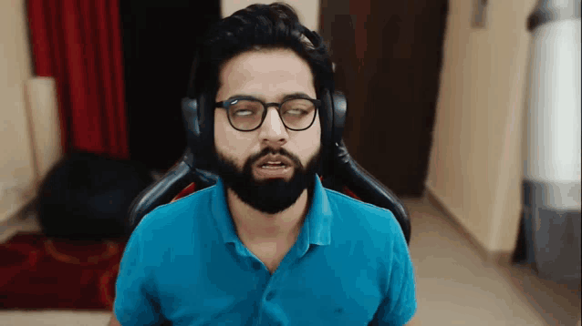 a man with glasses and a beard is wearing headphones and a blue shirt