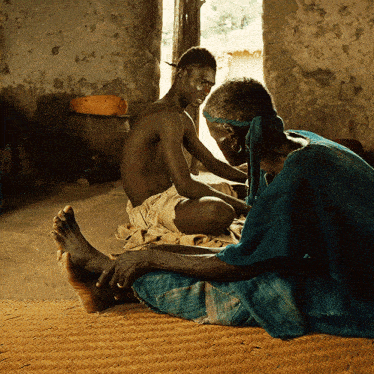 a man in a blue shirt sits next to a shirtless man