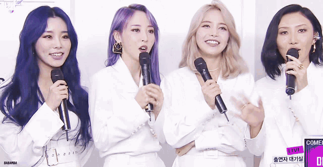 a group of women standing next to each other with microphones and a sign that says come live on it