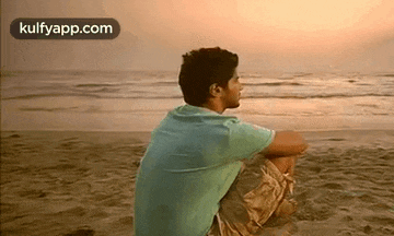 a man is sitting on the beach and looking at the ocean .