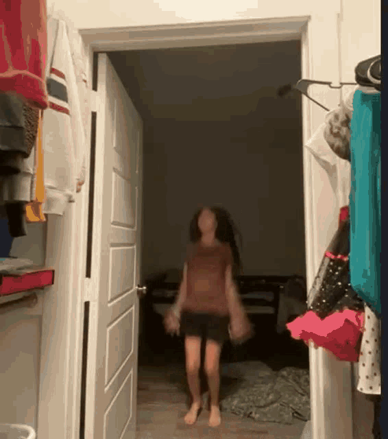 a girl is walking through a doorway in a room with clothes hanging on the wall .