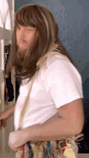 a man with long hair and a white shirt is standing in a doorway