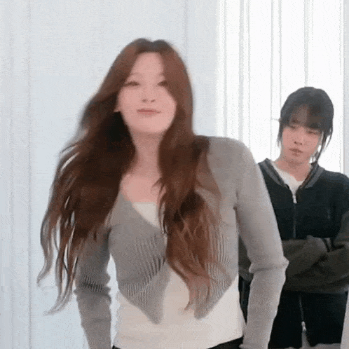 two women are standing next to each other in a room . one of the women is wearing a gray cardigan .