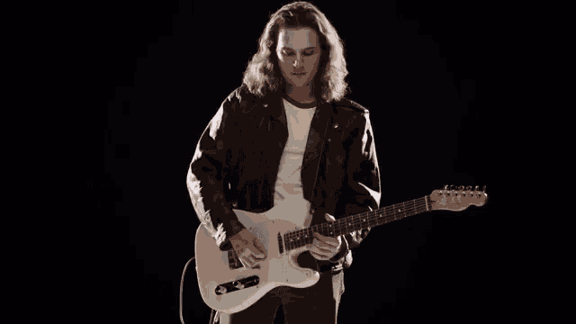 a young man with long hair is playing a white electric guitar .