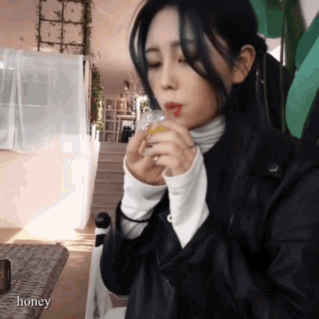 a woman in a black leather jacket drinking from a glass with the word honey below her