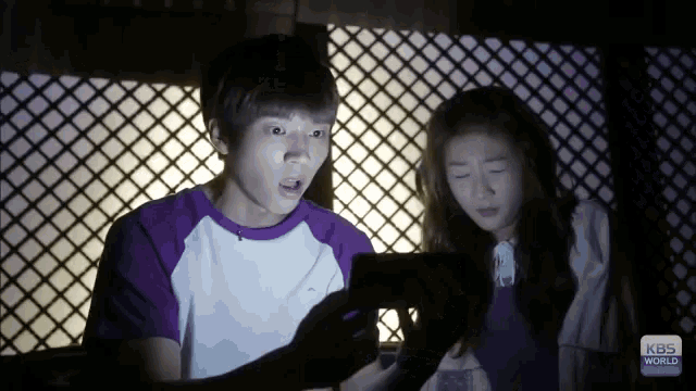 a boy and a girl looking at a cell phone with kbs world written on the bottom right
