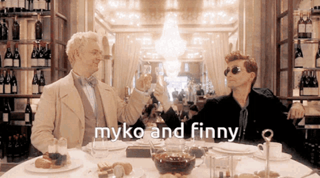 two men sitting at a table toasting with the words myko and finny
