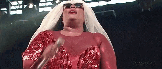 a woman in a red dress is singing into a microphone while wearing sunglasses and a white veil .