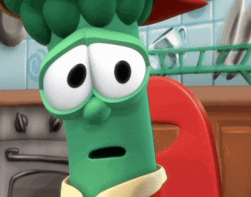a green cartoon character with big eyes is sitting in a kitchen
