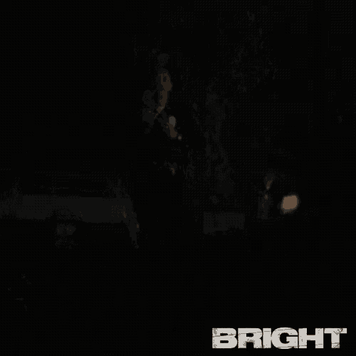 a man in a police uniform is standing in the dark in front of a car with the word bright on it
