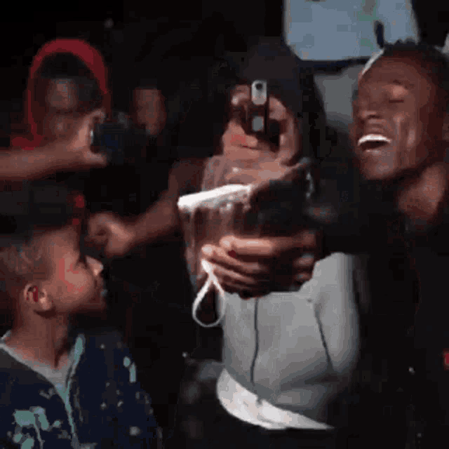 a group of people are standing in a dark room laughing and taking pictures with their phones .
