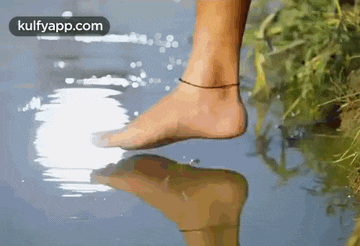 a person 's foot is standing in a puddle of water with a reflection of their foot in the water .