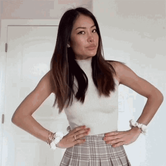 a woman with her hands on her hips is wearing a plaid skirt and a white top