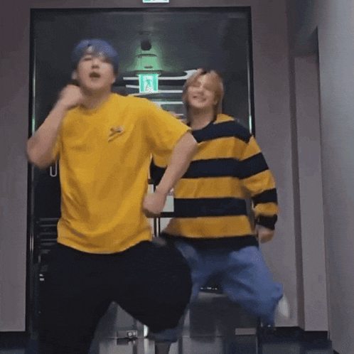 a man in a yellow shirt and a man in a black and yellow striped shirt are dancing together in a hallway .
