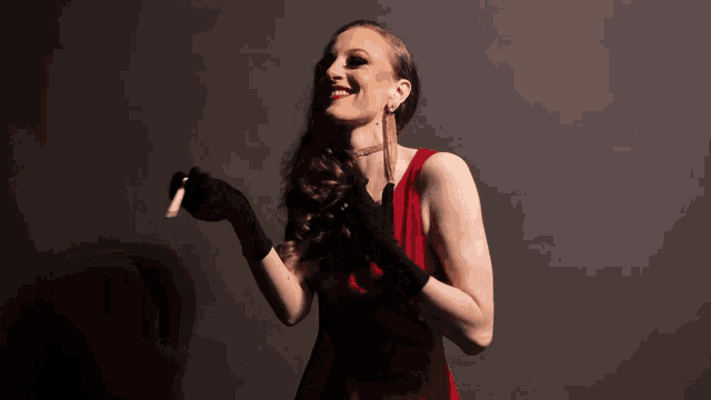 a woman in a red dress and black gloves is holding a cigarette