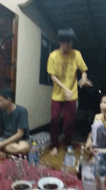 a man in a yellow shirt is dancing in front of a table
