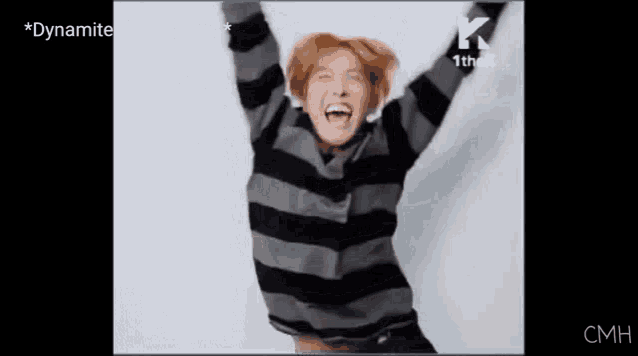 a man in a striped sweater is laughing and raising his arms in the air .
