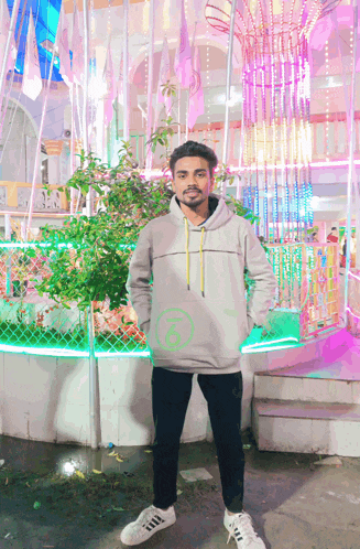 a man wearing a grey hoodie and white adidas shoes stands in front of a colorful display