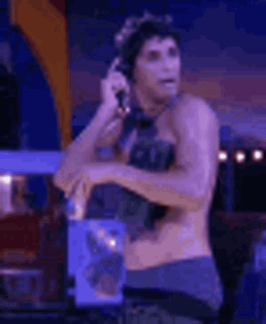 a shirtless man is talking on a cell phone while standing in front of a microphone .
