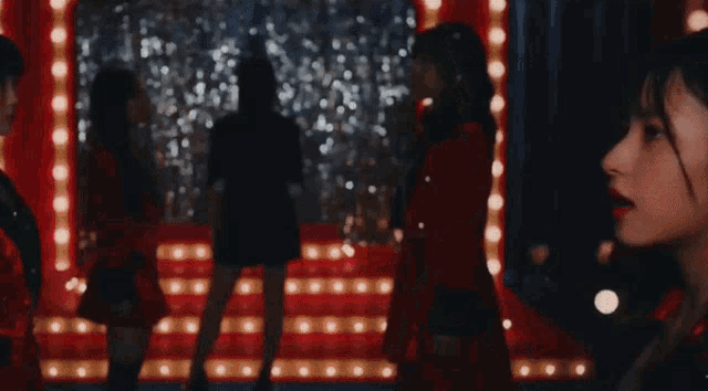 a group of women in red dresses are dancing on a stage with lights