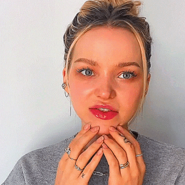 a close up of a woman 's face with many rings on her hands