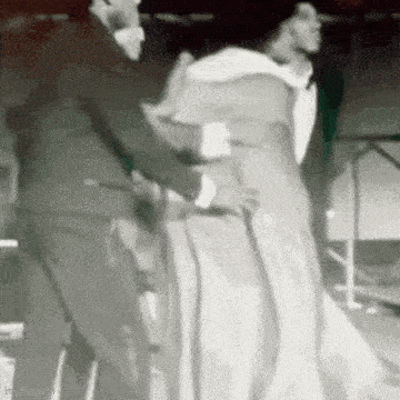 a man in a suit is helping a woman in a white dress with a cane .