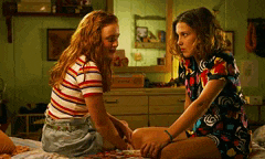 two young women are sitting on a bed talking to each other .