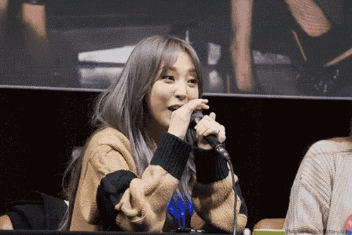 a woman is singing into a microphone while wearing a brown sweater