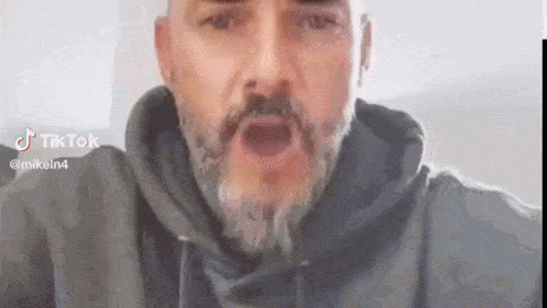a man with a beard is wearing a black hoodie and talking to the camera .