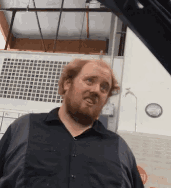 a man with a beard wearing a black shirt is standing in front of a clock