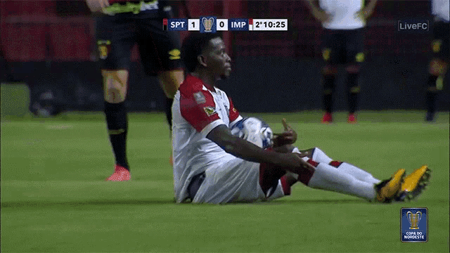 a soccer player sits on the ground during a game with the score being 0 to 0
