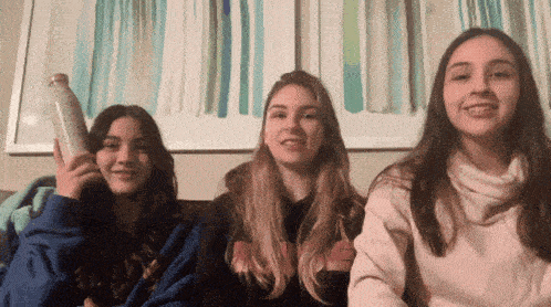 three girls sitting on a couch with one wearing a sweatshirt that says ' nirvana ' on it