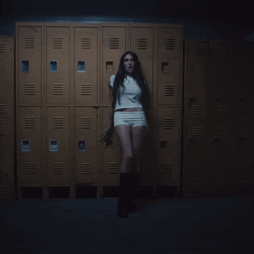 a woman standing in front of a wall of lockers in a dark room